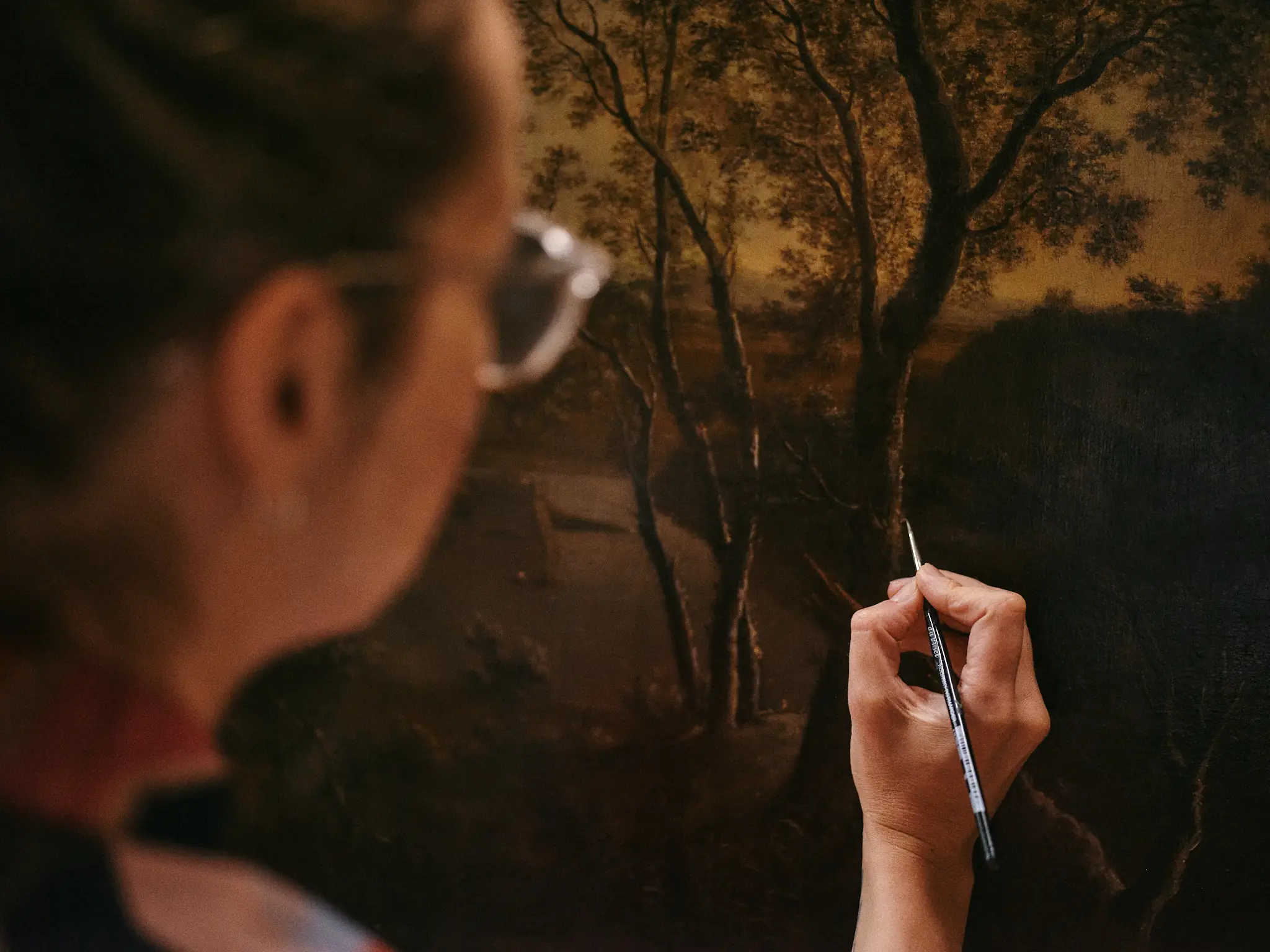 A photo of a restorer retouching a painting.